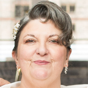 A smiling white woman wearing an elegant hair clip and earrings with her grey hair tied back. 